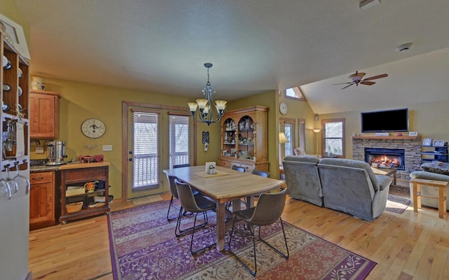 dining room featuring vaulted ceiling, a stone fireplace, a wealth of natural light, and light wood-style flooring