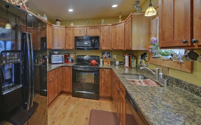 kitchen with brown cabinetry, light wood-style flooring, black appliances, pendant lighting, and a sink