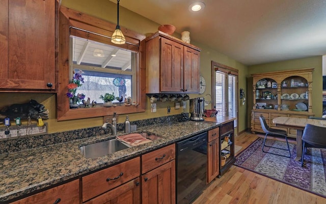 kitchen with light wood finished floors, dishwasher, dark stone countertops, decorative light fixtures, and a sink