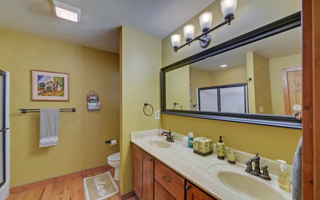 bathroom featuring double vanity, a shower with door, a sink, and wood finished floors