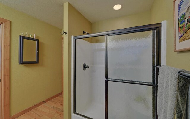 full bathroom featuring a shower with door, baseboards, and wood finished floors