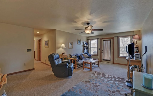 living area featuring light carpet, ceiling fan, a textured ceiling, and baseboards