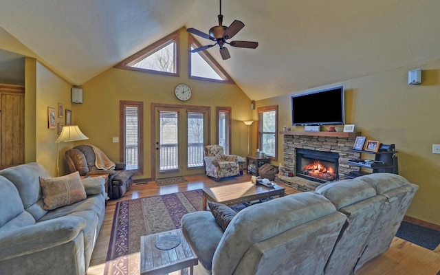 living area featuring ceiling fan, high vaulted ceiling, a stone fireplace, light wood-style flooring, and baseboards