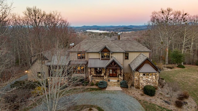 view of front facade with a mountain view, covered porch, stone siding, and a chimney