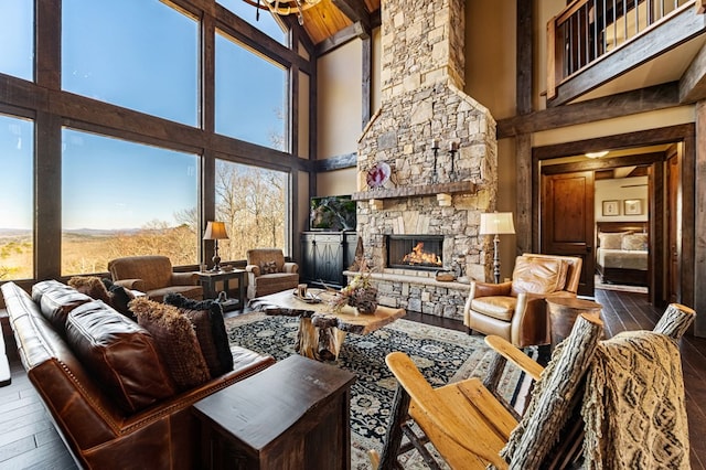 living room with a stone fireplace, wood finished floors, a healthy amount of sunlight, and a towering ceiling