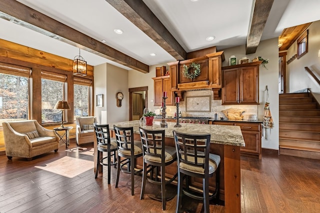 kitchen featuring backsplash, dark wood-style floors, a breakfast bar area, light stone countertops, and hanging light fixtures