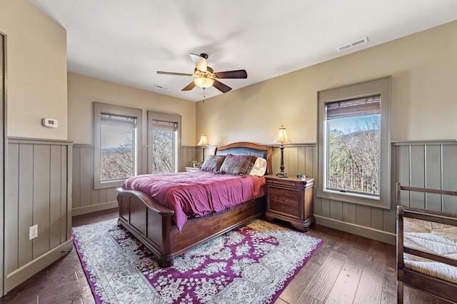 bedroom with hardwood / wood-style floors, visible vents, a wainscoted wall, and a ceiling fan