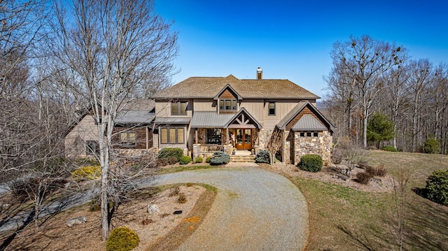 view of front of house with gravel driveway, covered porch, a chimney, french doors, and stone siding