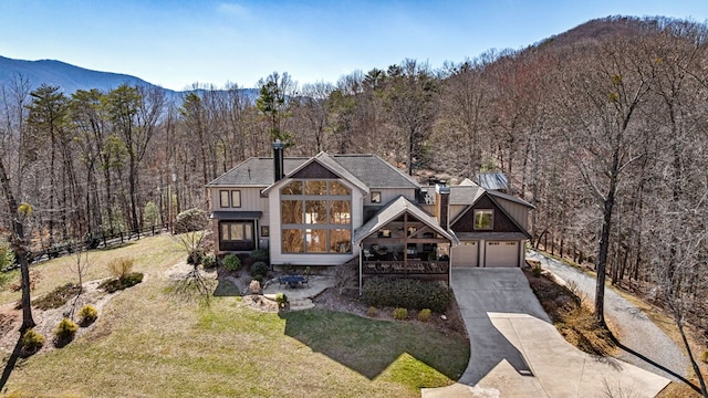 view of front facade with board and batten siding, a forest view, fence, a front yard, and driveway