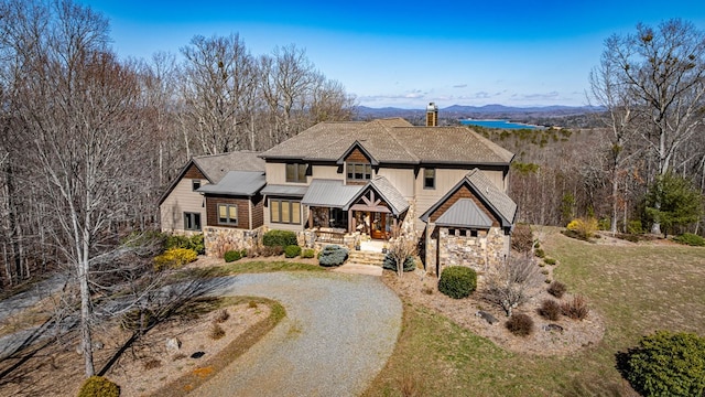 view of front of home with stone siding, a chimney, and driveway