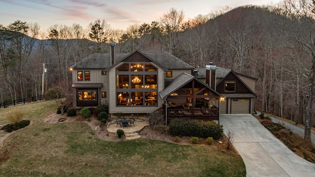 view of front of home featuring a wooded view, fence, concrete driveway, a lawn, and a chimney