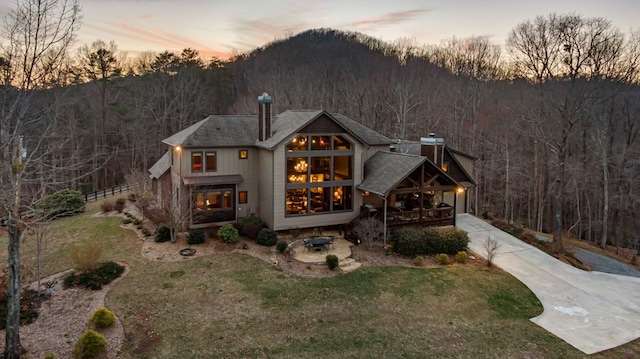 back of property featuring a forest view, a yard, and concrete driveway