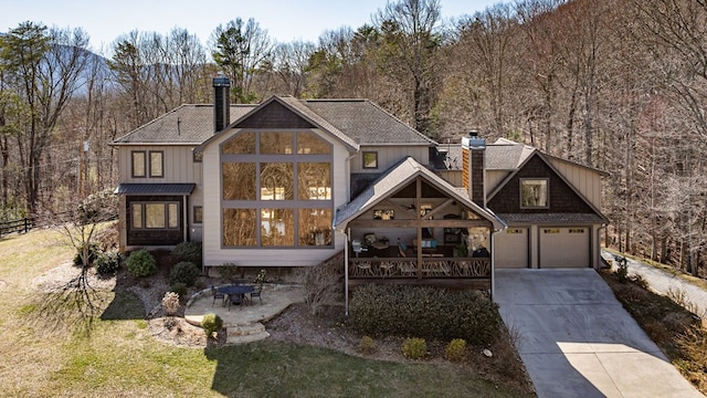 view of front of home with fence, a wooded view, an attached garage, concrete driveway, and a chimney