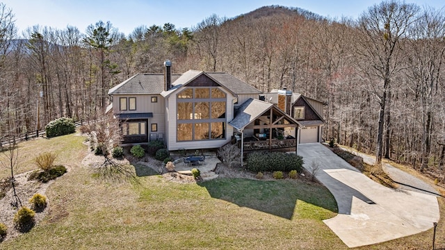 view of front of home with a forest view, concrete driveway, and a front lawn