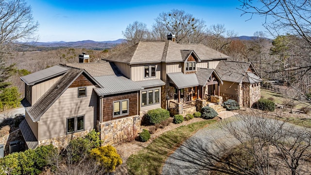 view of front of house featuring roof with shingles, a mountain view, a chimney, stone siding, and board and batten siding