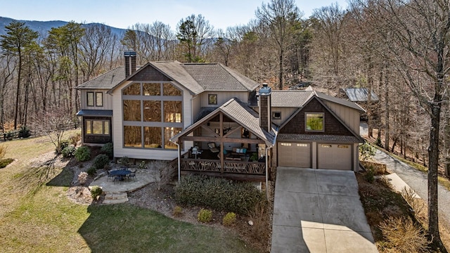 view of front of house featuring driveway, a wooded view, a chimney, and a shingled roof