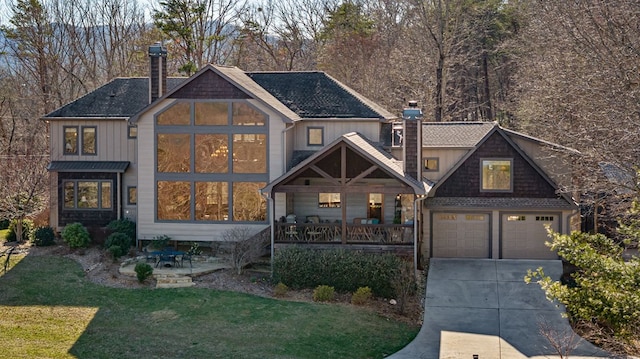 view of front of home with a front lawn, a porch, concrete driveway, and a chimney