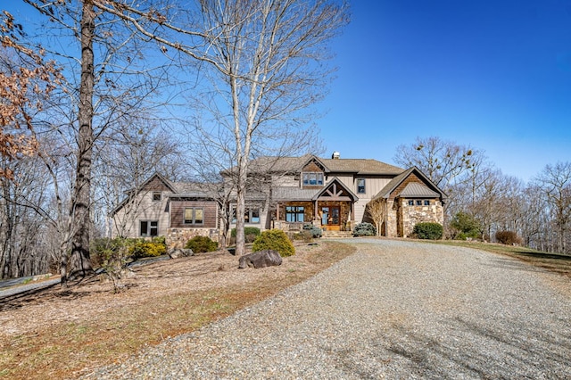 view of front of home with stone siding, gravel driveway, covered porch, board and batten siding, and a chimney