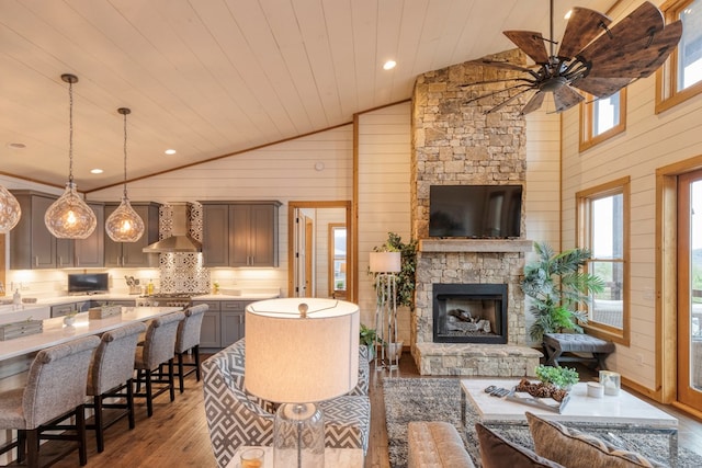 living room featuring a ceiling fan, wood walls, an outdoor stone fireplace, lofted ceiling, and hardwood / wood-style floors