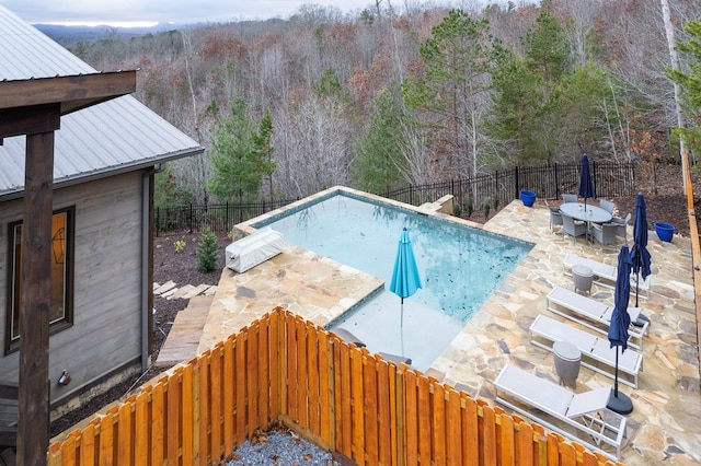 view of swimming pool featuring a fenced in pool, a fenced backyard, a patio area, and a forest view