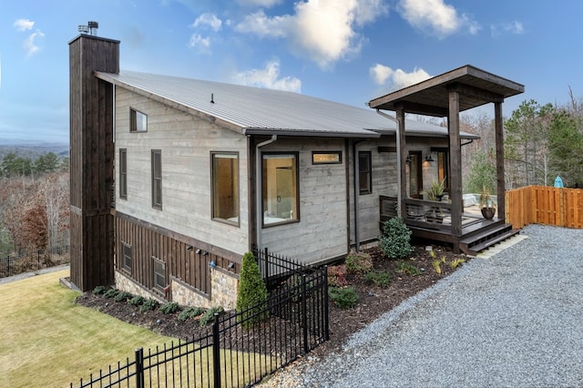 view of front facade featuring fence, stone siding, a deck, a chimney, and metal roof