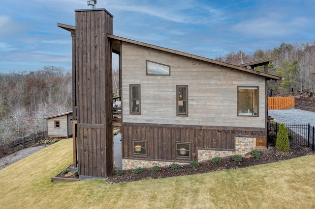 view of property exterior with a lawn, fence, and stone siding