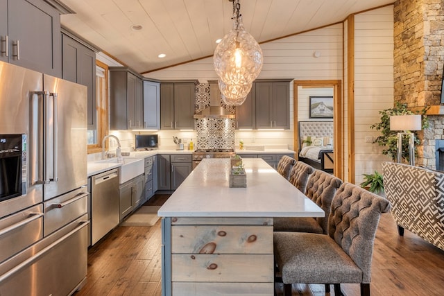 kitchen featuring lofted ceiling, a kitchen island, wall chimney range hood, high quality appliances, and gray cabinetry