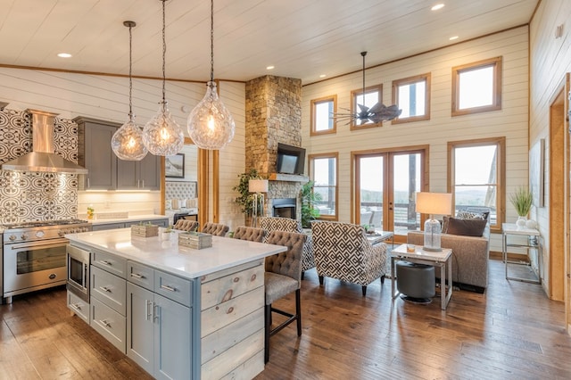 kitchen with open floor plan, light countertops, gray cabinets, wall chimney exhaust hood, and stainless steel appliances