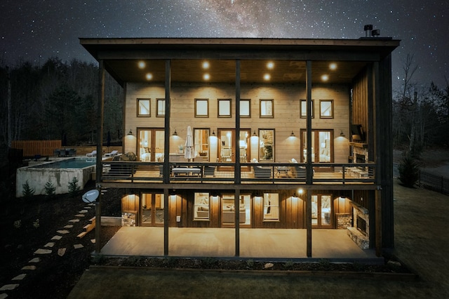 back of house at twilight featuring french doors, a patio, and board and batten siding