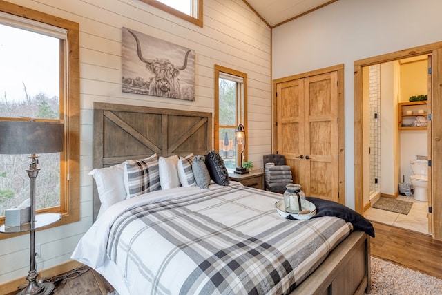 bedroom featuring wooden walls, vaulted ceiling, wood finished floors, and ensuite bath