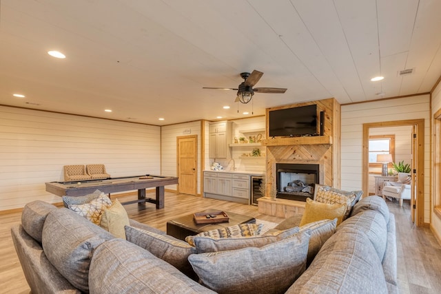 living area featuring beverage cooler, wood walls, light wood finished floors, and a fireplace