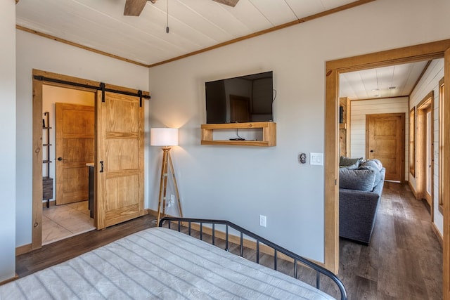 bedroom featuring crown molding, baseboards, a barn door, and wood finished floors