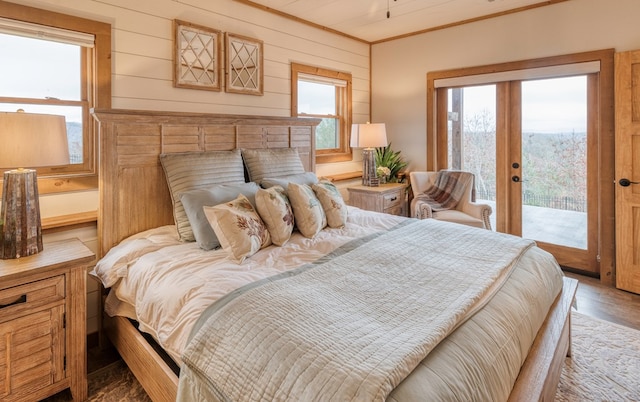 bedroom with ornamental molding, wood finished floors, access to exterior, wooden walls, and french doors