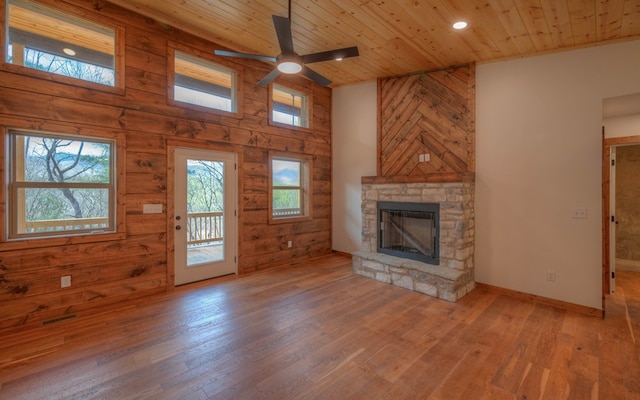 unfurnished living room with ceiling fan, plenty of natural light, wood-type flooring, and a stone fireplace