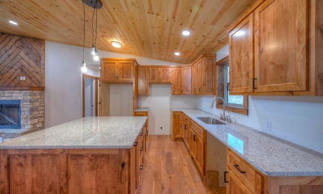 kitchen featuring hanging light fixtures, sink, light stone countertops, a stone fireplace, and light hardwood / wood-style floors