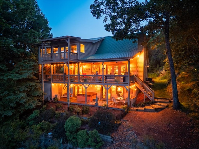 back house at dusk with a balcony, a wooden deck, a jacuzzi, and a patio