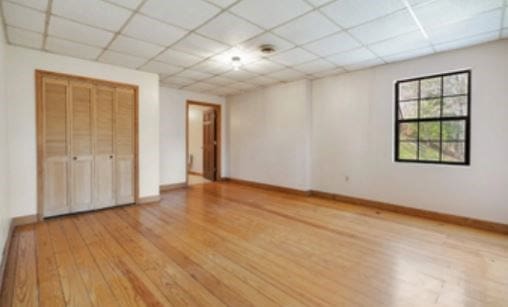 unfurnished bedroom with a drop ceiling, light wood-style flooring, and baseboards