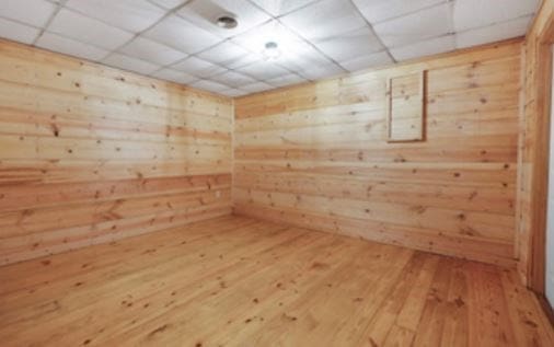 spare room featuring a sauna, wooden walls, a drop ceiling, and hardwood / wood-style floors