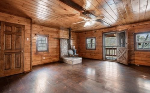 interior space featuring ceiling fan, wooden ceiling, wooden walls, wood finished floors, and a wood stove