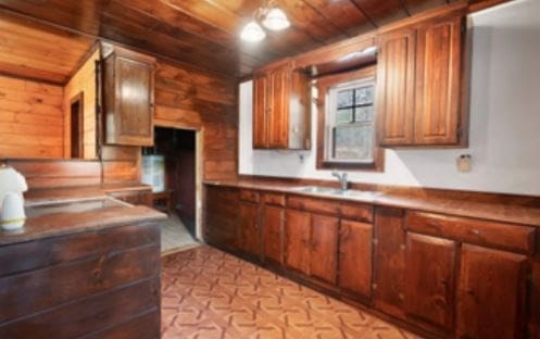 kitchen with wood ceiling, wooden walls, brown cabinetry, and a sink