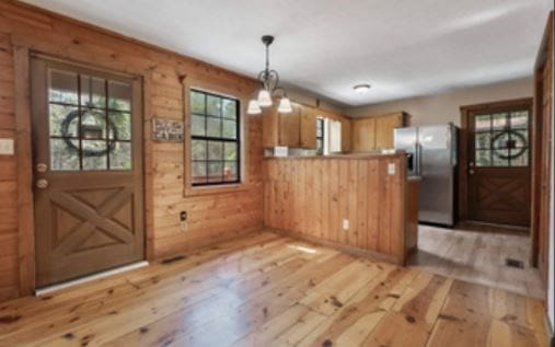 kitchen with light wood finished floors, hanging light fixtures, wooden walls, a peninsula, and stainless steel fridge with ice dispenser