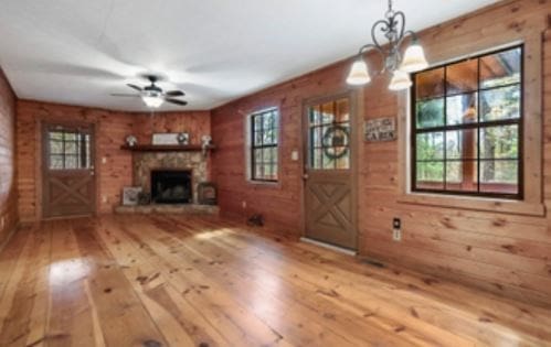 unfurnished living room with plenty of natural light, wooden walls, a fireplace with raised hearth, and hardwood / wood-style floors