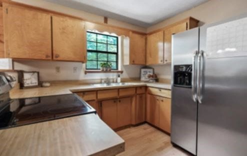 kitchen featuring a sink, black electric range, light countertops, light wood-type flooring, and stainless steel refrigerator with ice dispenser