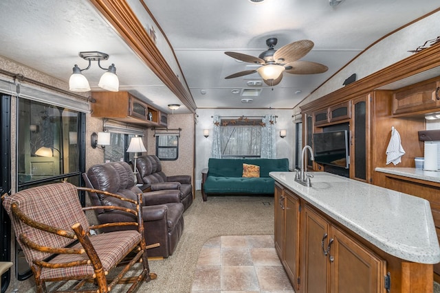 kitchen with light stone countertops, a textured ceiling, light colored carpet, ceiling fan, and a center island with sink