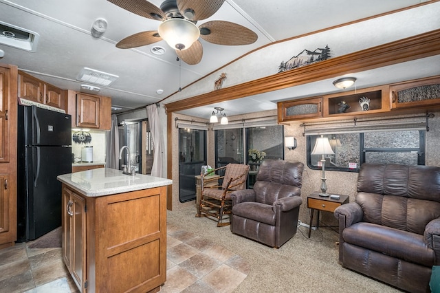 kitchen with a center island with sink, black refrigerator, light stone countertops, and vaulted ceiling