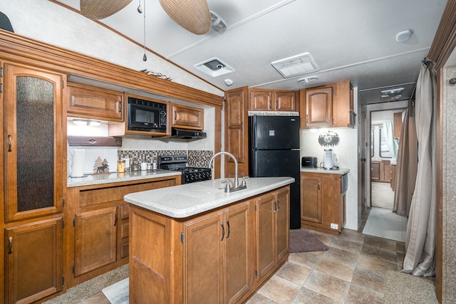 kitchen with vaulted ceiling, ceiling fan, sink, black appliances, and an island with sink