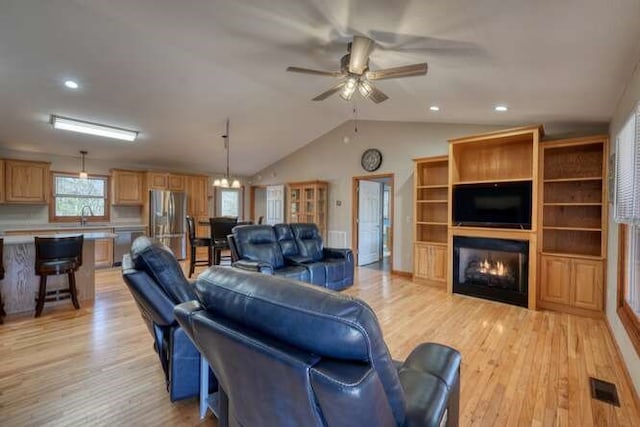 living area with visible vents, a ceiling fan, light wood-style flooring, a lit fireplace, and vaulted ceiling