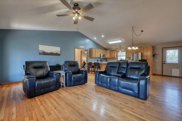 living room featuring vaulted ceiling, ceiling fan with notable chandelier, light wood-style flooring, and baseboards