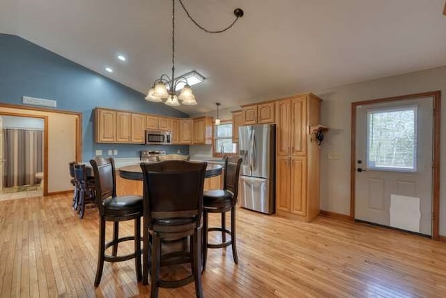 kitchen featuring light wood-style flooring, a kitchen island, vaulted ceiling, stainless steel appliances, and a chandelier