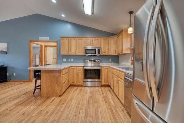 kitchen with stainless steel appliances, a breakfast bar, light brown cabinets, and a peninsula